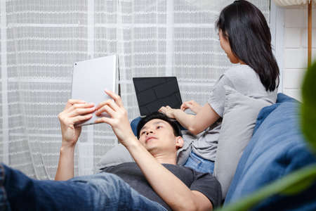 Asian young couple Sit and relax on their blue sofa in their home during the holidays. Family concept, work at home.の写真素材