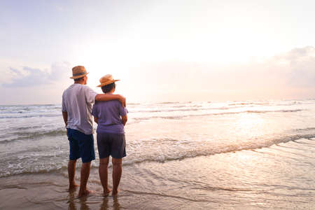 An elderly Asian couple Stand together on the beach Look at the beautiful sea in the morning together. Travel concept to live happily in retirement age. copy spaceの写真素材