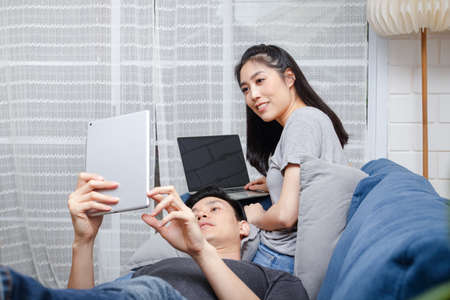 Asian young couple Sit and relax on their blue sofa in their home during the holidays. Family concept, work at home.の写真素材