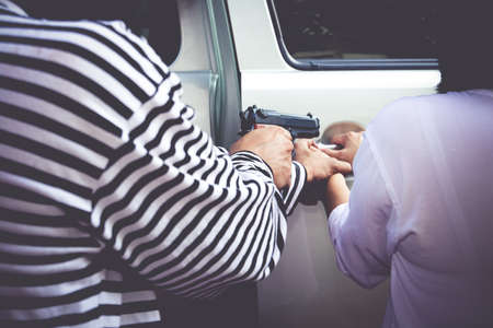 Car thieves hold a gun to rob a car from a woman who owns it. Close-up photo. Insurance concept....