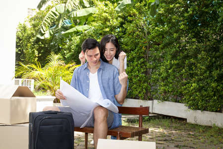 Asian men and women couples holding a sheet of paper blueprints for the construction of a new house...