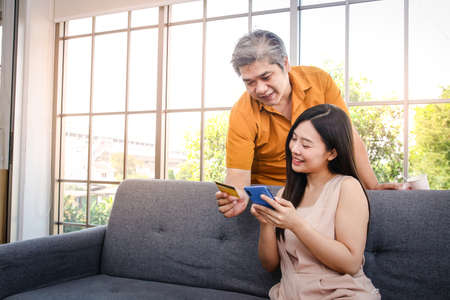 Asian couple holding credit card and smartphone to order online instead of going out of the house. Self-defense, stay at home during the coronavirus spread. social distanceの写真素材