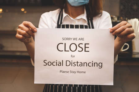 young woman wearing a mask running a coffee shop business Hold a white paper banner with a message of closing the shop and social distancing. Entrepreneurs Doing Business During the Coronavirus Spreadの写真素材