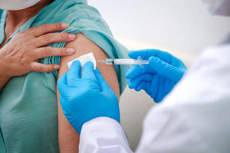 Close-up portrait of an elderly woman receiving coronavirus vaccination from a male doctor wearing blue gloves To strengthen the immune system to prevent infection. Elderly Vaccinationの写真素材