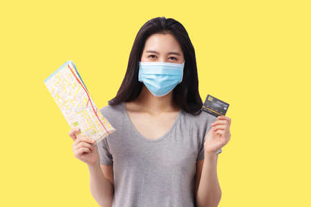 Asian woman with long hair wear a mask Hold a travel map and credit card. To prepare for domestic...
