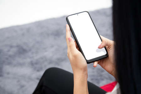 woman holding a black smartphone with a white screen Sit on the sofa in the living room. online...