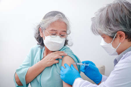 Close-up portrait of an elderly woman receiving coronavirus vaccination from a male doctor wearing...