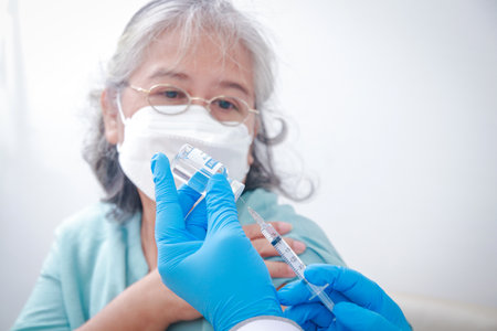 Close-up portrait of an elderly woman receiving coronavirus vaccination from a male doctor wearing blue gloves To strengthen the immune system to prevent infection. Elderly Vaccinationの写真素材
