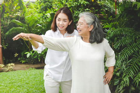 Asian elderly woman doing physical therapy Has a daughter to help support in stretching the arms. They were both in the garden in front of the house. concept of caring for the elderly to be healthyの写真素材