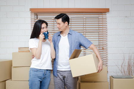 Asian couple moving into a new home There were many large brown cardboard boxes placed in the room. family concept happy couple feel satisfied Moved to a new house to build a family.の写真素材