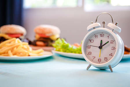 The white clock shows lunch time. There are hamburgers and fries on the table. fast food conceptの写真素材
