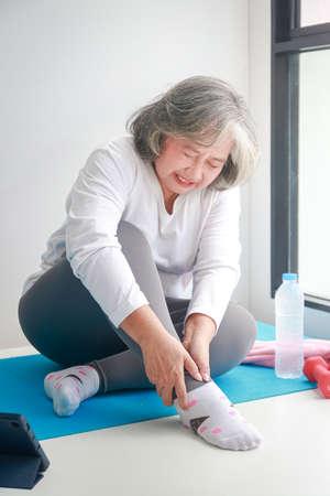 Asian elderly woman exercising at home Injured on the right ankle. There is a lot of pain. concept of health care for seniors.の写真素材