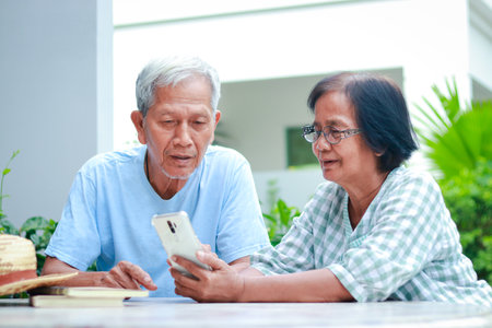 Asian elderly couple happy living at home Sitting in the garden holding a smartphone, chatting...