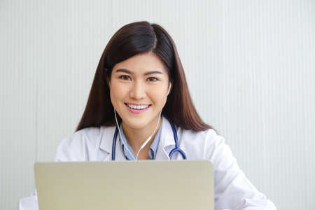 Asian female doctor online video call Check the symptoms with the patient via the Internet. on a laptop computer. The concept is connected to communication through online technology.の写真素材