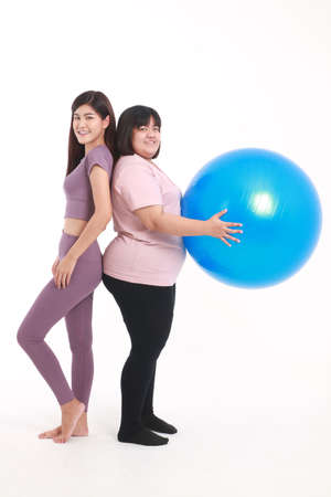 A skinny Asian woman and a fat woman stand next to each other. Put on exercise clothes, play yoga ball. on a white background. weight loss exercise conceptの写真素材