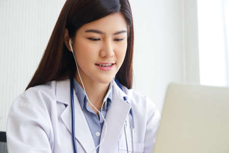 Asian female doctor online video call Check the symptoms with the patient via the Internet. on a laptop computer. The concept is connected to communication through online technology.の写真素材