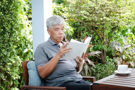Asian elderly man sitting and relaxing Read a book on the balcony of his house. The concept of taking care of the health of seniors in retirement to be happy.の写真素材