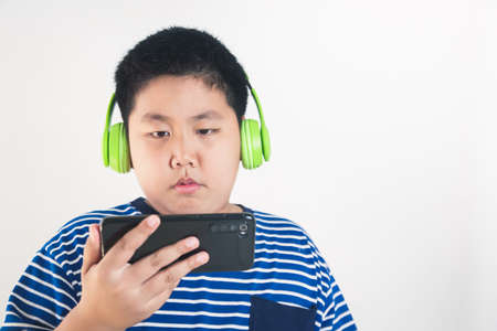 Asian fat boy wearing headphones and holding a smartphone Learn online through video calls with teachers. distance education concept use modern technology During the epidemicの写真素材