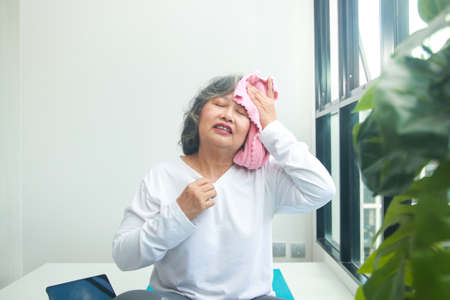 Asian elderly woman exercising at home Take a pink cloth to wipe the sweat. Exercises to maintain health for the elderly. concept of social distancingの写真素材