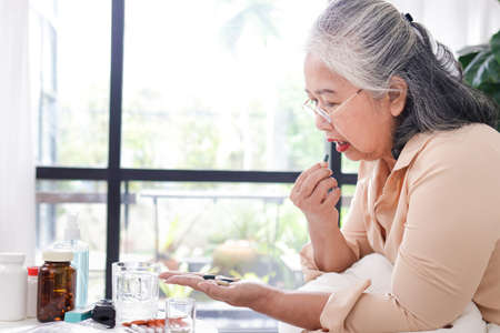 Asian elderly woman stay home to prevent infection During the virus epidemic She was sick with a fever and took medication to treat the virus. Home isolation concept, stay at homeの写真素材
