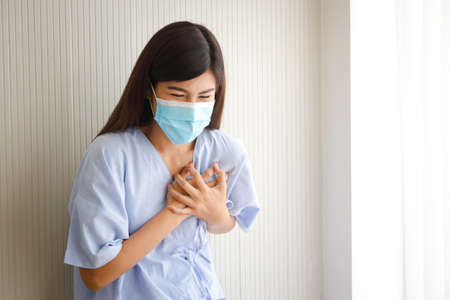female patient wearing a mask have heart pain Put your hand on your chest to reduce the pain. Cardiovascular disease in working women aged 35 years and over. Hospital concept. medical servicesの写真素材
