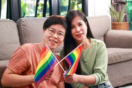 Asian lesbian couples live together at home in the living room. Carrying the LGBT symbol flag. Young same-sex married couples living together.の写真素材