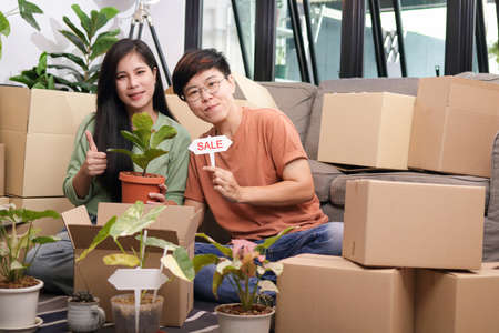 An Asian lesbian couple runs an online plant selling business. Help pack it into a cardboard box and send it to the customer. The concept of married young same-sex couples living together.の写真素材