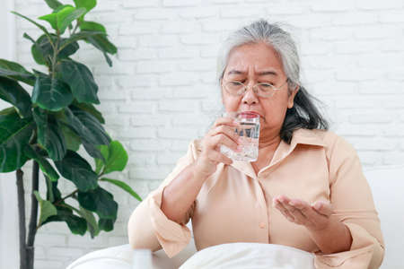 Asian elderly woman stay at home She has a flu. She is taking painkillers and drinking plain water. The concept of disease of the elderly.の写真素材