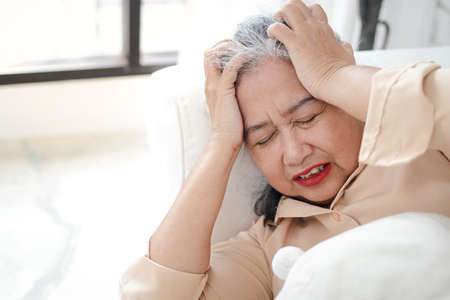 Asian elderly woman lying sick on the sofa in the living room She had a huge headache. concept of home treatment, health care for the elderly. Copy spaceの写真素材