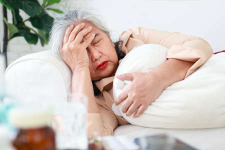 Asian elderly woman lying sick on the sofa in the living room She had a huge headache. concept of home treatment, health care for the elderlyの写真素材