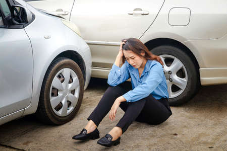 Asian woman sitting stressed Had an accident driving a car into the side of another car Because the road is slippery, it rains. Insurance concept, drive carefully in Thailand rainy seasonの写真素材