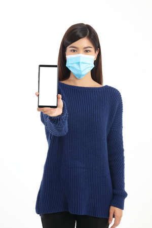 beautiful asian woman wearing a blue mask Standing holding a black smartphone with a white screen. White background. Concept of using modern technology in communication. online talk to doctorの写真素材