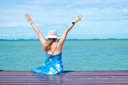 50 year old Asian woman sitting on a wooden floor by the sea She raised both hands, enjoying the sea during the holidays. Concept of natural tourism in Thailandの写真素材