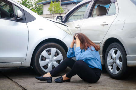 Asian woman sitting stressed Had an accident driving a car into the side of another car Because the road is slippery, it rains. Insurance concept, drive carefully in Thailand rainy seasonの写真素材