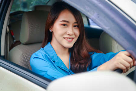 Beautiful Asian woman driving a car to work. She smiled happily. The concept of driving carefully in the rainy season in Thailandの写真素材