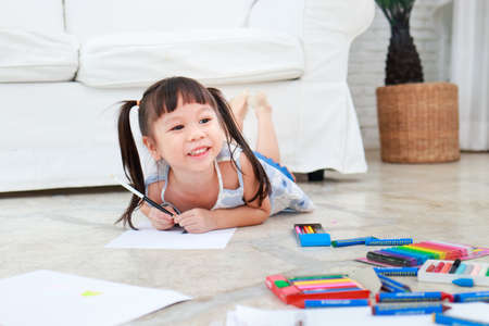 cute little asian girl smiling happy Lay down drawing on the floor in the living room of the house....