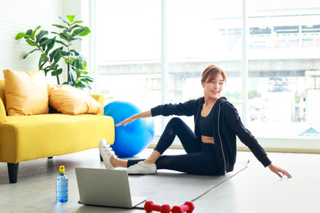 beautiful asian woman Exercise in the living room in the apartment She did the exercises following the trainer through online videos on her laptop computer. Health care concept, new normalの写真素材