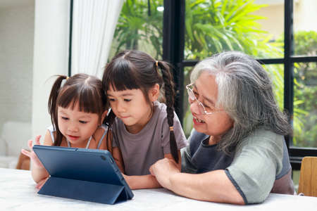 Asian grandmother and two granddaughters Study online on a tablet. Online education during the coronavirus pandemic. home isolation. Family concept.の写真素材