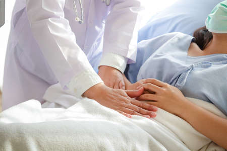 Doctors hold a woman's stomach area lying in hospital bed to check for symptoms of illness. concept of treating patients during the coronavirus pandemic, medical servicesの写真素材