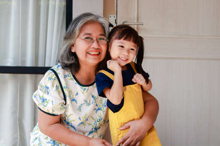 elderly grandmother with cute little granddaughter live at home together. Grandma dressed her granddaughter for school in the morning. educational concepts of kindergarten childrenの写真素材