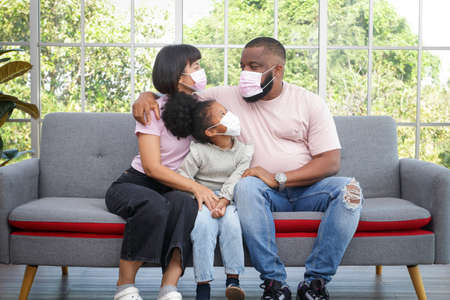 black family Parents and daughters sit on the sofa in the living room. They wear masks to prevent the . Health care concept, social distancing to prevent germsの写真素材