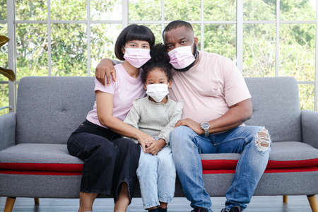black family Parents and daughters sit on the sofa in the living room. They wear masks . Health care concept, social distancing to prevent germsの写真素材