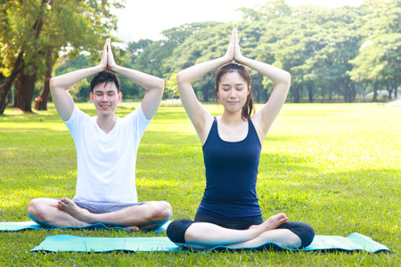 Asian couple exercising In the morning, sit and do yoga on the green grass in the outdoor park. they smile happy healthy. fitness concept, health careの写真素材