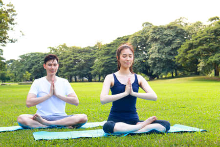 Asian couple exercising In the morning, sit and do yoga on the green grass in the outdoor park. they smile happy healthy. fitness concept, health careの写真素材