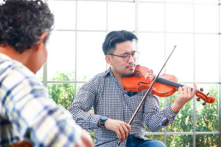 two asian men playing the violin classical instrument and acoustic guitar together in the music practice room The couple enjoyed playing acoustic music. Concept of playing live music and bandの写真素材