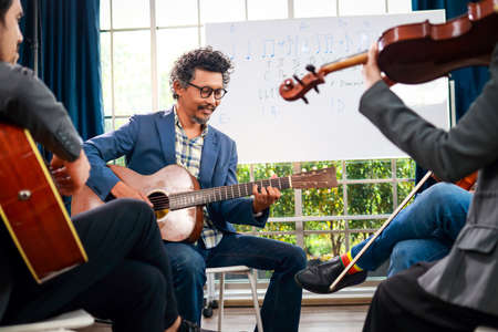 A group of Asian musicians playing guitar and violin sitting on classical music. They are fun and happy. Concept of learning classical music. Live music and bandsの写真素材