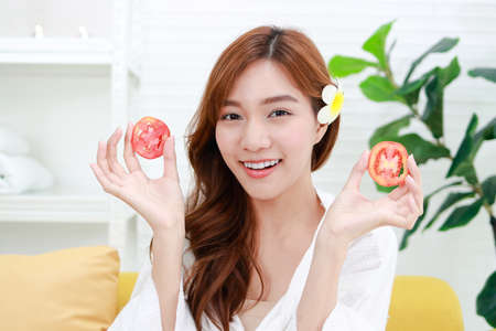 Beautiful Asian woman doing spa at home She holds a tomato to mask her face, making her face clear. Beauty concept. For good health, make the body comfortable, relaxed and beautiful.の写真素材