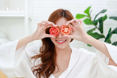 Beautiful Asian woman doing spa at home She holds a tomato to mask her face, making her face clear. Beauty concept. For good health, make the body comfortable, relaxed and beautiful.の写真素材