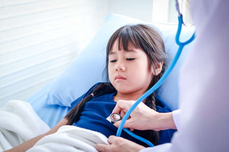 Female doctor holding a stethoscope to check the health of a cute little Asian girl lying on the bed. concept of medical services in hospitals, pediatric epidemicの写真素材
