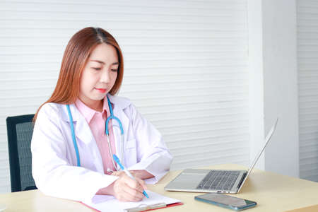 Asian female doctor sitting in office She is taking notes on auscultation. concept of medical services in a hospitalの写真素材
